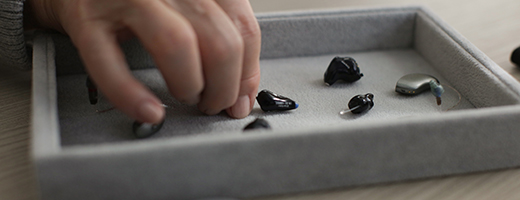 Image of hand choosing a hearing aid from several in a box.